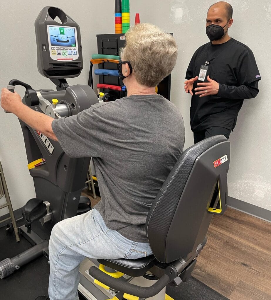 Adult physical therapy patients working on cardiovascular and strength training equipment under therapist supervision